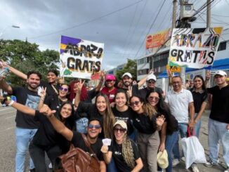 Jóvnes cristianos ofrecen abrazos con cartel de "Abrazos Gratis", en medio de una multitud colorida.