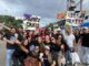 Jóvnes cristianos ofrecen abrazos con cartel de "Abrazos Gratis", en medio de una multitud colorida.