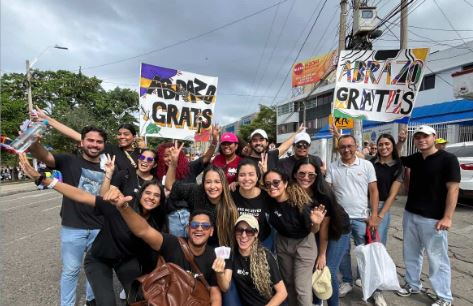 Jóvnes cristianos ofrecen abrazos con cartel de "Abrazos Gratis", en medio de una multitud colorida.